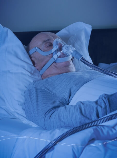 En mand, der sover i sengen, mens han trækker vejret gennem et respirationsapparat.