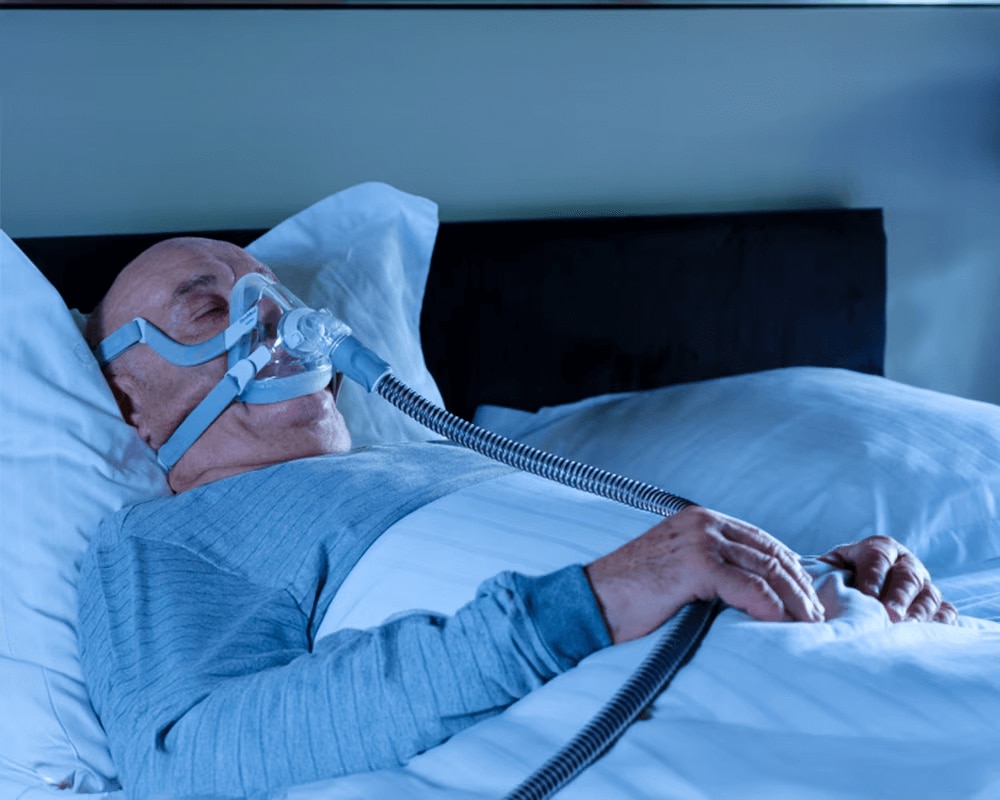 En mand, der sover i sengen, mens han trækker vejret gennem en ventilator.